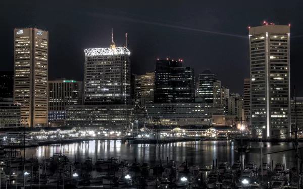 A stunning HD wallpaper showcasing the vibrant Baltimore skyline at night, with illuminated skyscrapers reflecting on the harbor's water, highlighting the city's urban charm.
