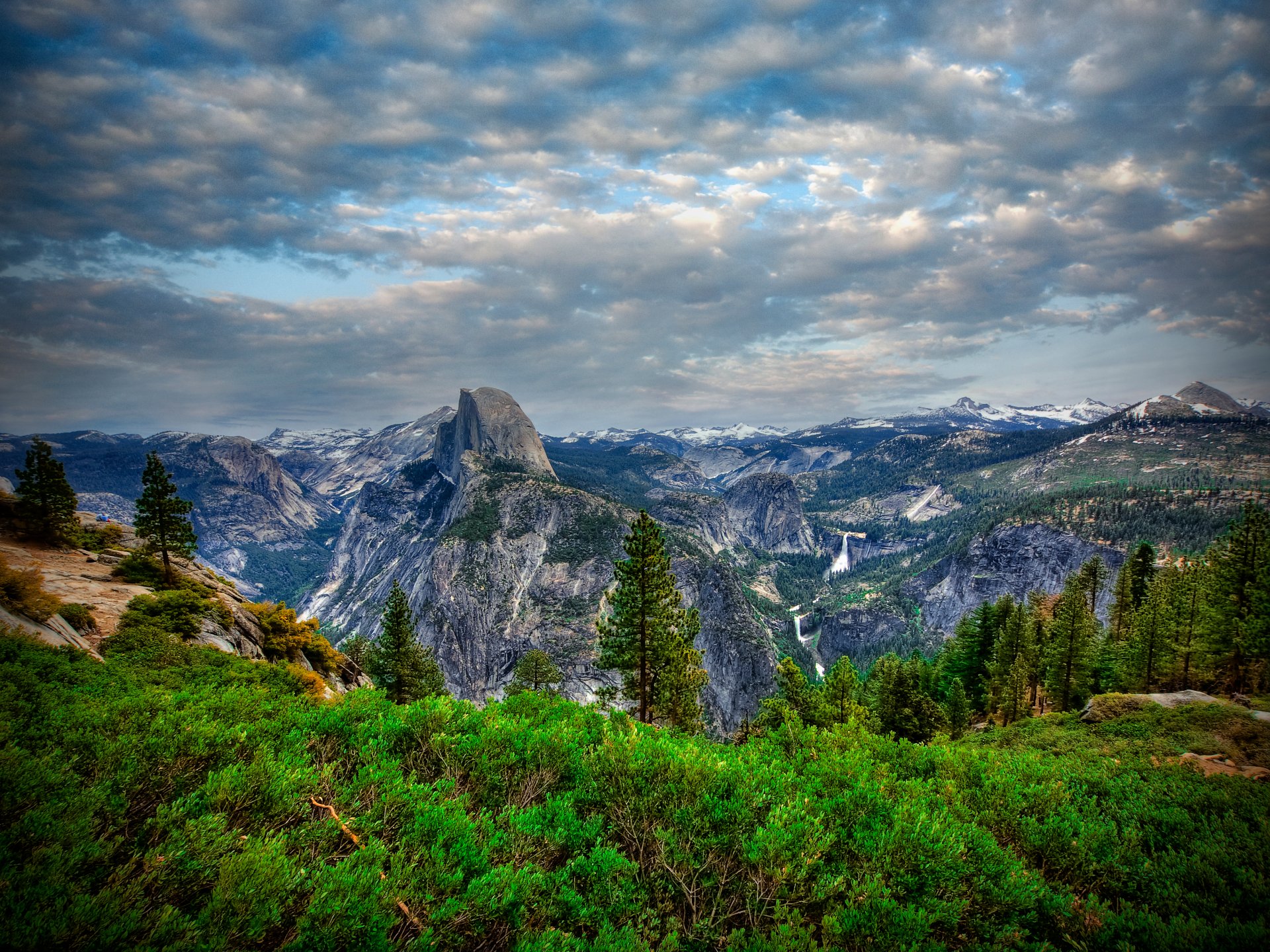 4K Ultra HD landscape of Yosemite National Park featuring dense forest, rugged mountains, and a dramatic cloudy sky, showcasing the park's natural beauty.