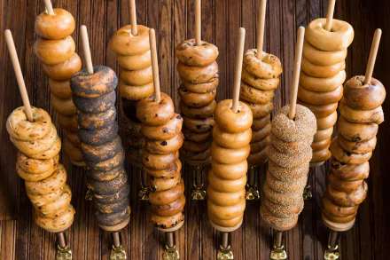 HD PC desktop wallpaper of assorted bagels (bread, food) threaded on vertical wooden skewers against a rustic wood background.