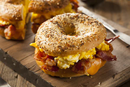 Close-up of a bacon, egg, and cheese bagel sandwich on a wooden board, captured in 4K Ultra HD quality for a PC desktop wallpaper and background.
