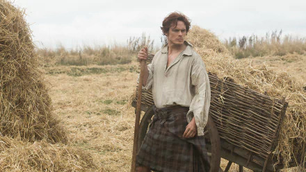 Kilted man in period costume standing beside a wooden cart in a hayfield — Outlander TV show HD desktop wallpaper/background.