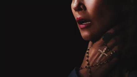A dark and suspenseful HD desktop wallpaper from the movie The Conjuring 2, featuring a close-up of a woman's face and a hand grasping a crucifix.