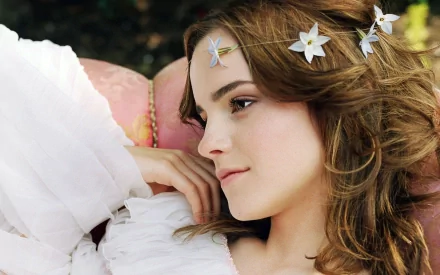HD desktop wallpaper featuring Emma Watson, wearing a delicate flower headband and a white dress, resting on a pink cushion.
