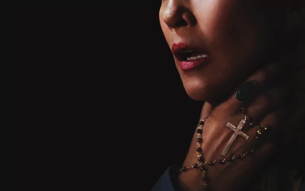 A dark and suspenseful HD desktop wallpaper from the movie The Conjuring 2, featuring a close-up of a woman's face and a hand grasping a crucifix.