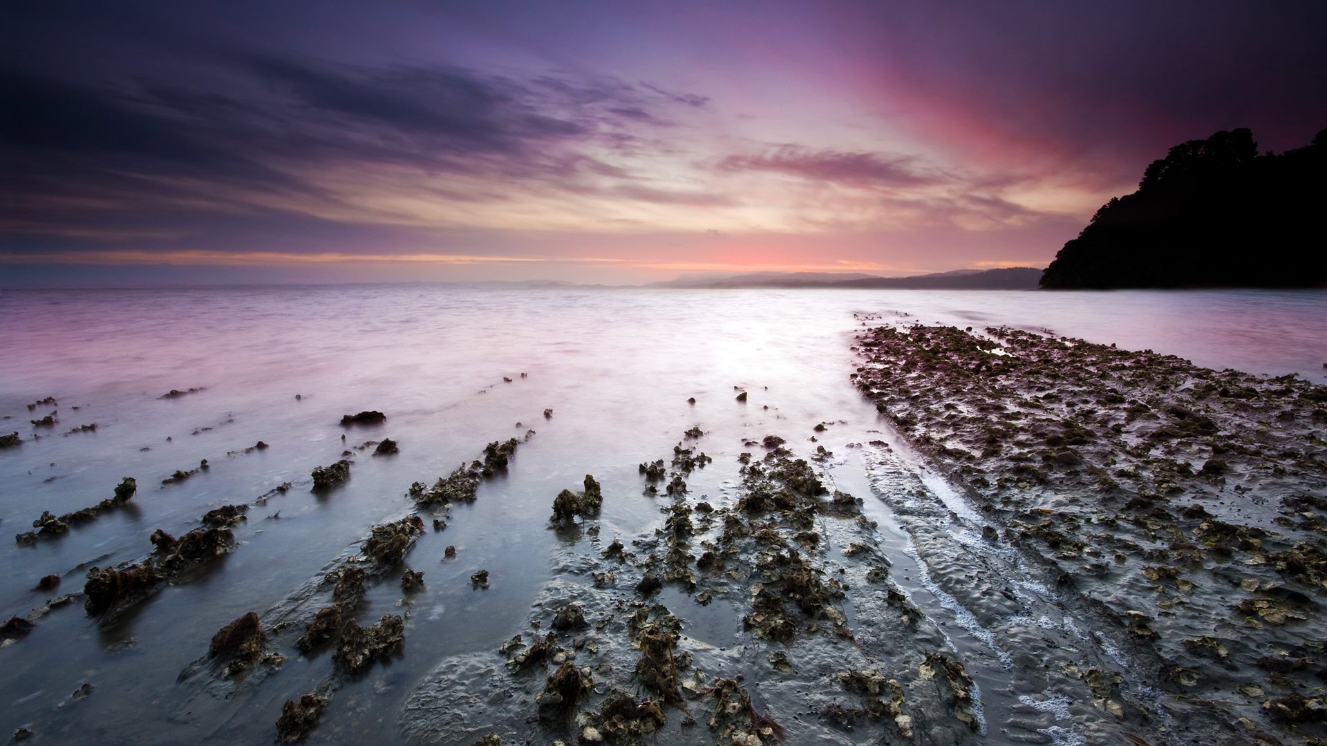 HD desktop wallpaper of a tranquil ocean scene at sunset, showcasing water and natural coastal landscape with soft purple and pink skies.