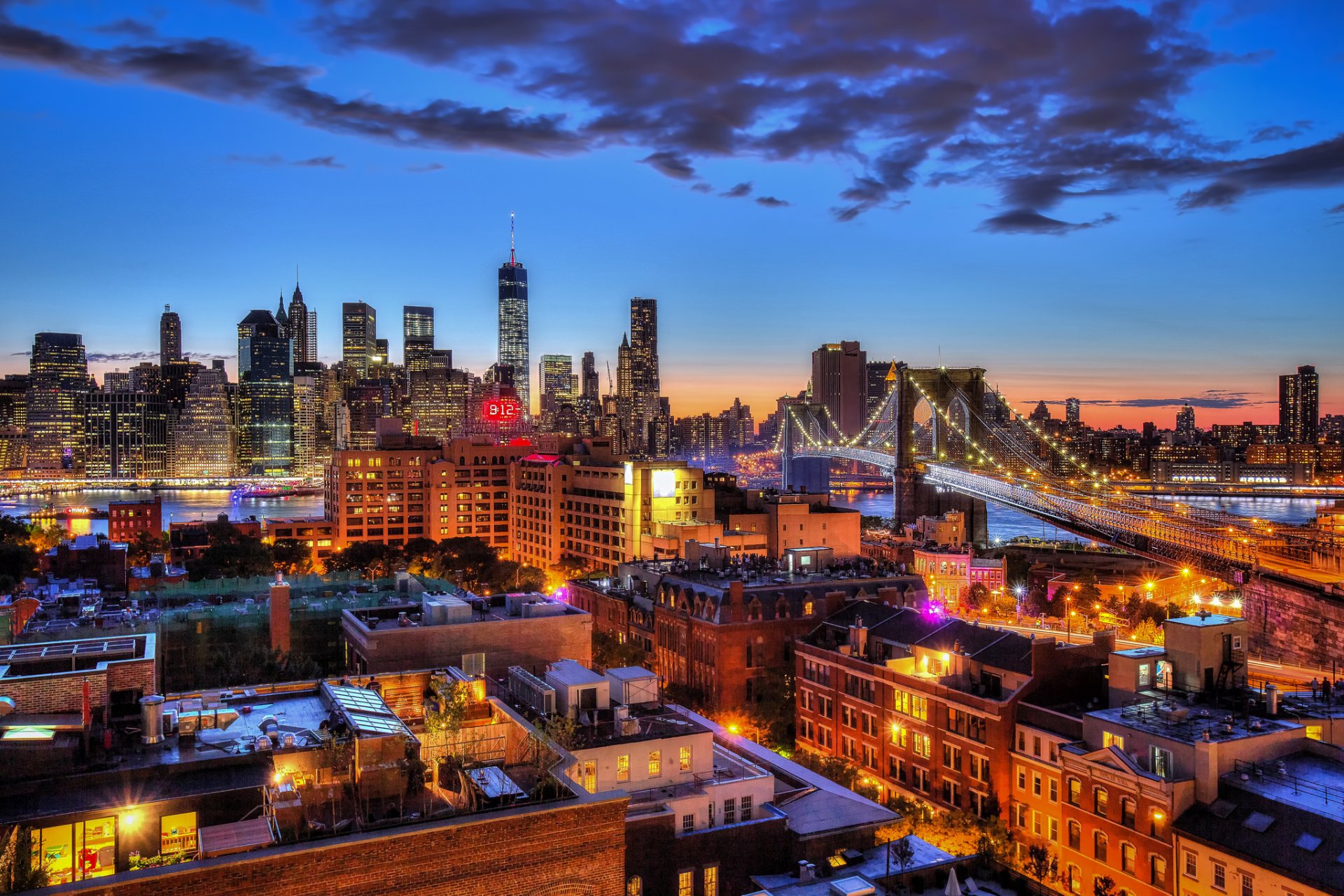 HD desktop wallpaper capturing New York City's illuminated skyscrapers and Brooklyn Bridge at night, showcasing vibrant city lights and the urban skyline.
