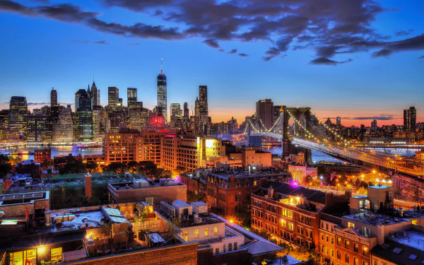 HD desktop wallpaper capturing New York City's illuminated skyscrapers and Brooklyn Bridge at night, showcasing vibrant city lights and the urban skyline.