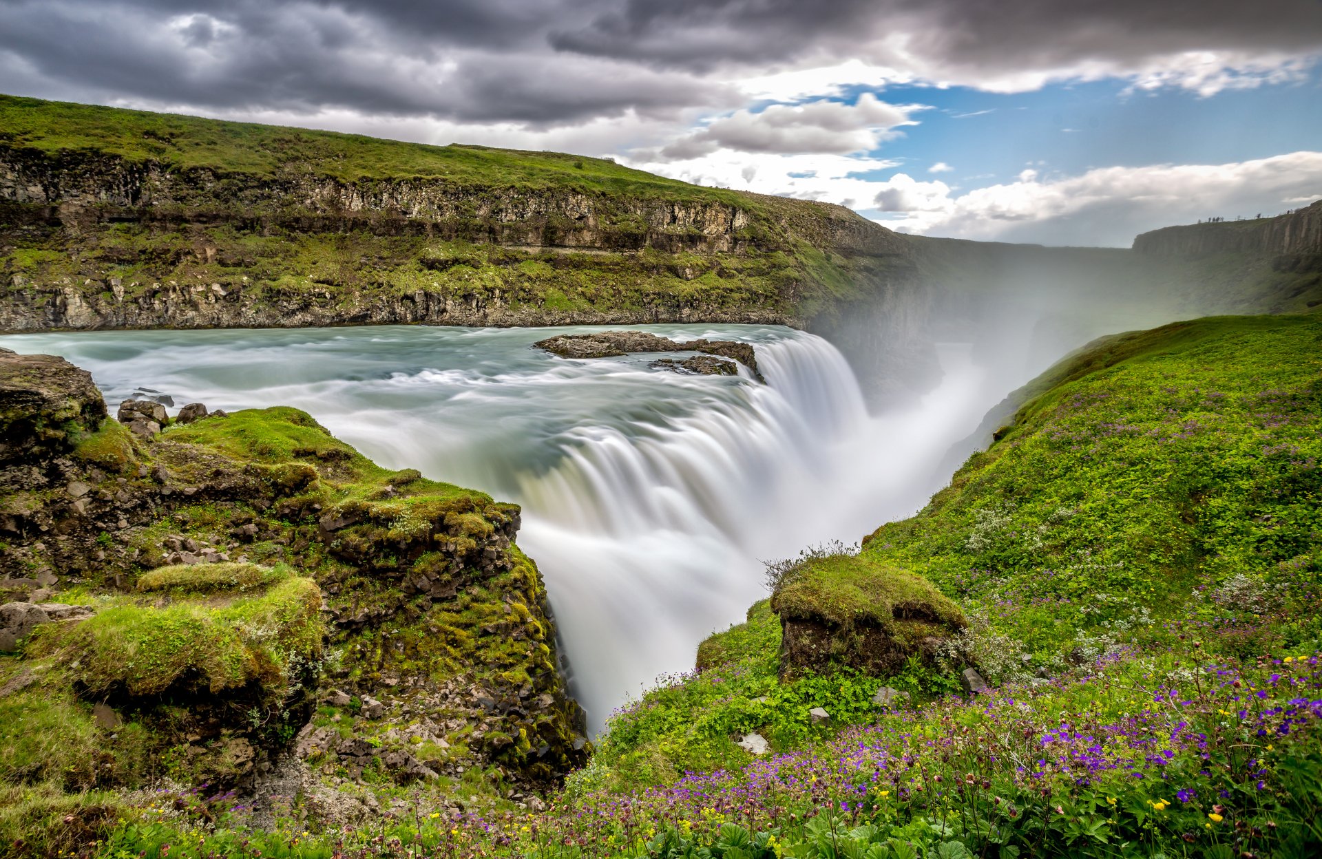 4K Ultra HD wallpaper of Iceland’s Gullfoss waterfall cascading through lush green cliffs under a partly cloudy sky.