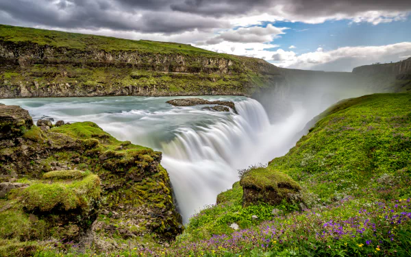 4K Ultra HD wallpaper of Iceland’s Gullfoss waterfall cascading through lush green cliffs under a partly cloudy sky.