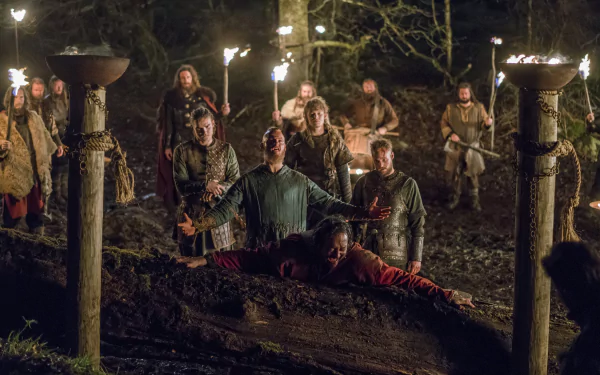 4K Ultra HD PC desktop wallpaper: Vikings (2013) — torchlit forest ritual with warriors and priests encircling a prone body on a funeral pyre, grim faces illuminated by braziers.
