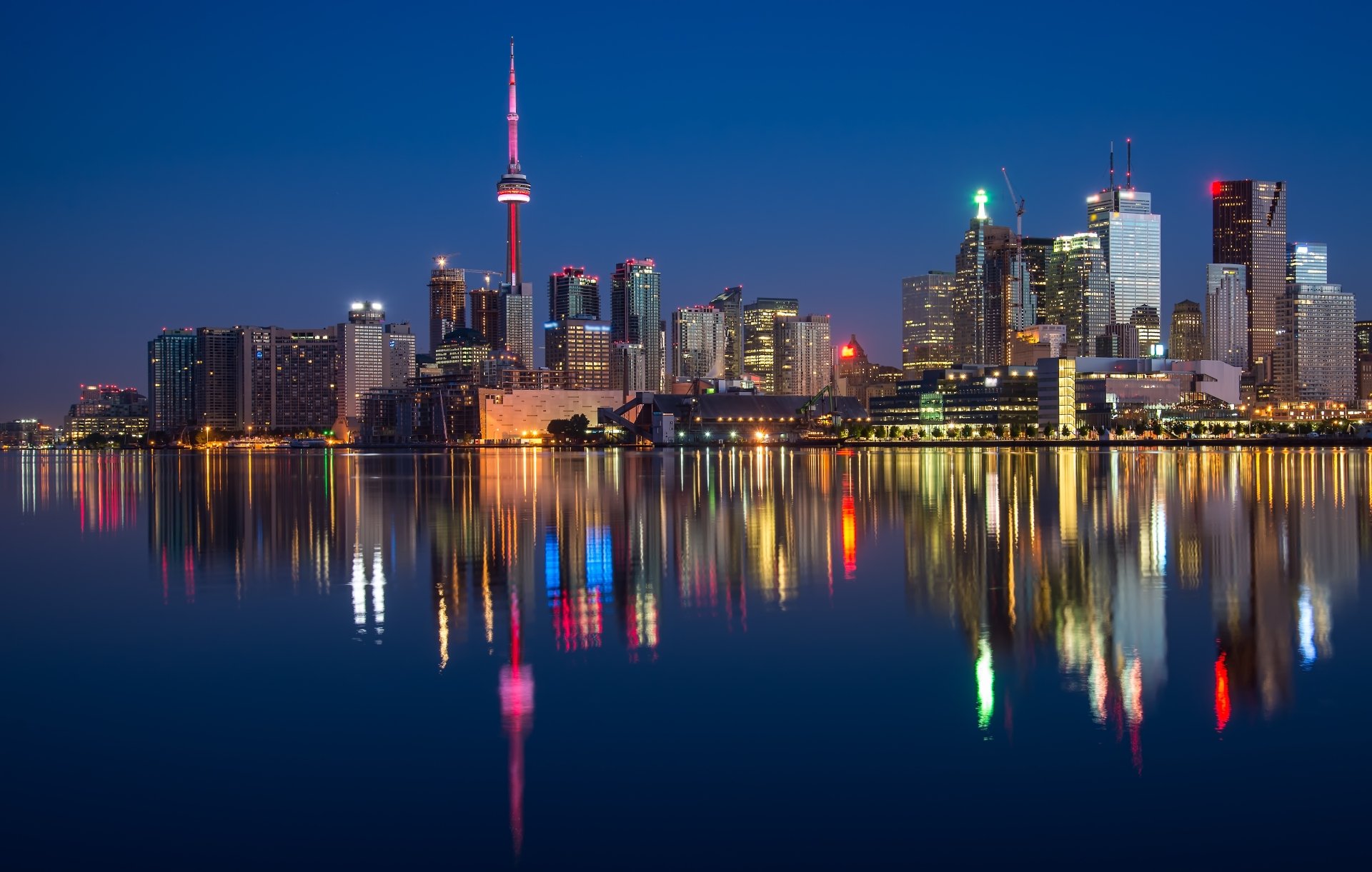A stunning nighttime view of Toronto's skyline, featuring skyscrapers reflecting vibrant lights on the calm waters, showcasing the beauty of Ontario, Canada.