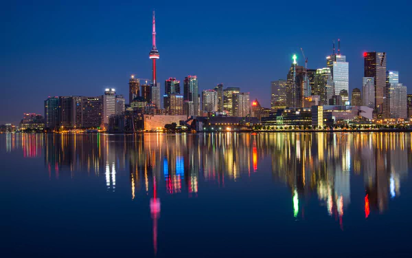 A stunning nighttime view of Toronto's skyline, featuring skyscrapers reflecting vibrant lights on the calm waters, showcasing the beauty of Ontario, Canada.