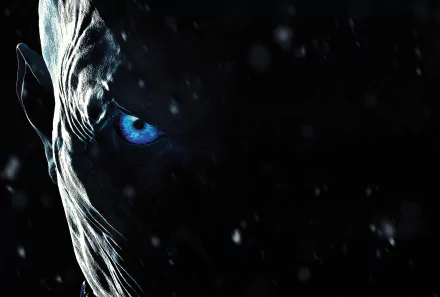 HD wallpaper of a White Walker from the TV show Game of Thrones, showcasing a close-up of its face with a glowing blue eye in a dark, snowy background.