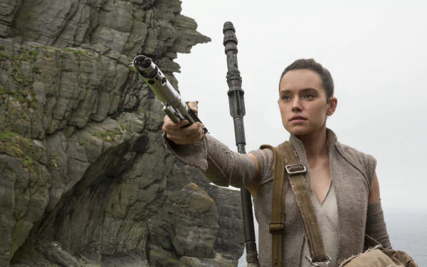 HD desktop wallpaper featuring Daisy Ridley as Rey from Star Wars: The Last Jedi. Rey is holding a lightsaber, positioned against a backdrop of rocky cliffs.