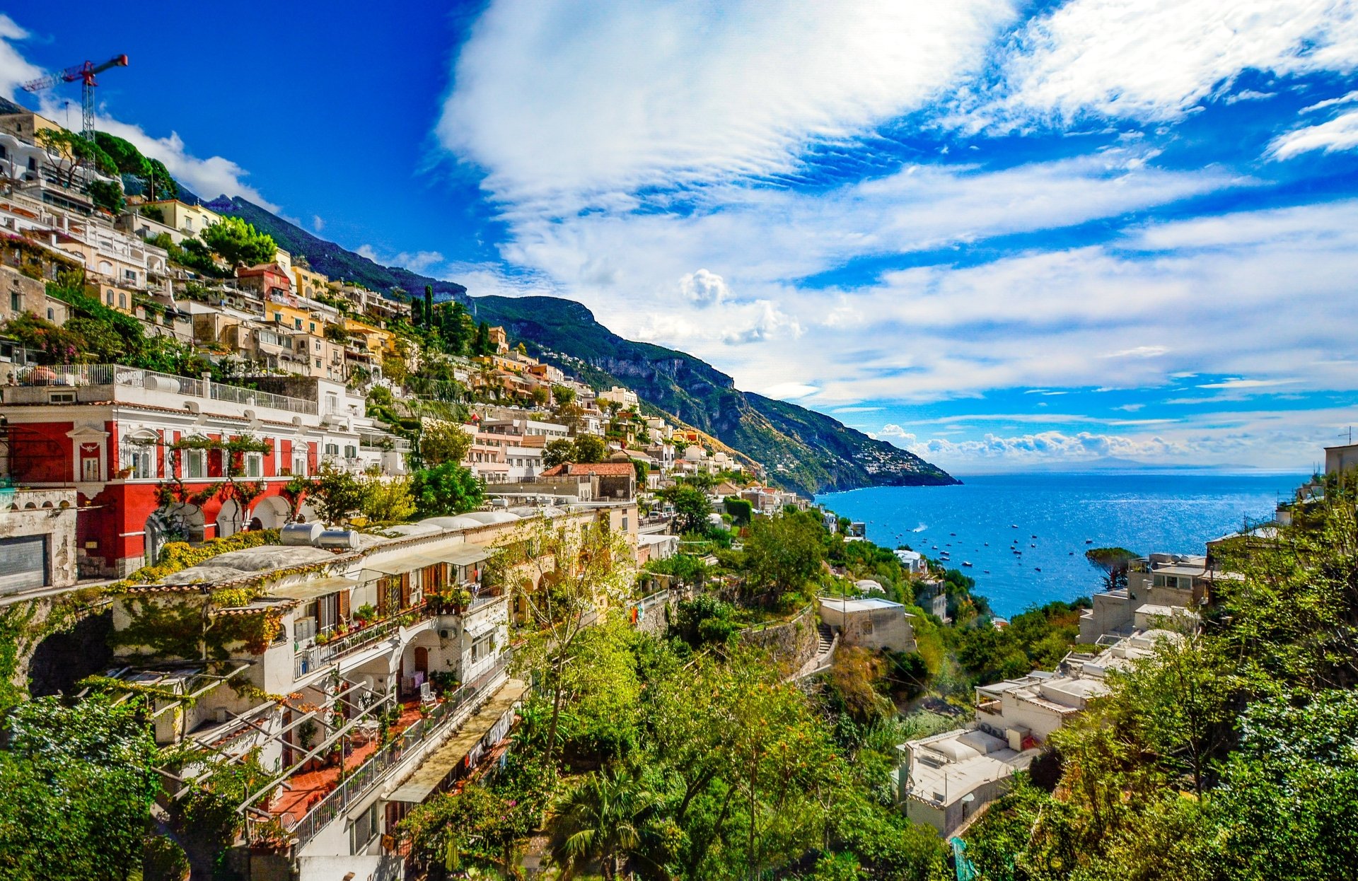 4K Ultra HD wallpaper of Amalfi Coast, Italy, featuring a vibrant town on cliffs overlooking the ocean, with lush greenery, houses, and a bright blue sky with clouds.