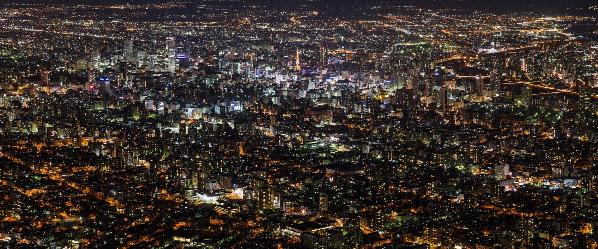 Aerial night view of Sapporo, Japan, showcasing a sprawling man-made cityscape illuminated across the horizon in stunning 4K Ultra HD detail.