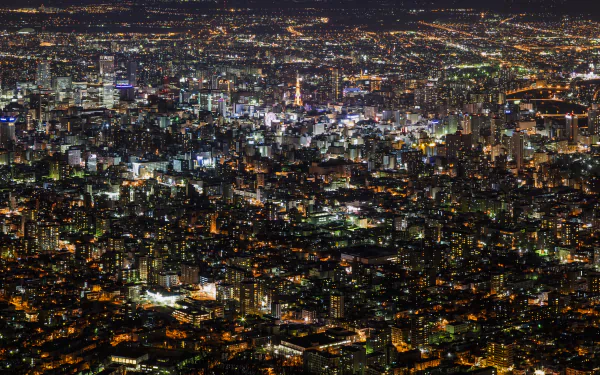 Aerial night view of Sapporo, Japan, showcasing a sprawling man-made cityscape illuminated across the horizon in stunning 4K Ultra HD detail.