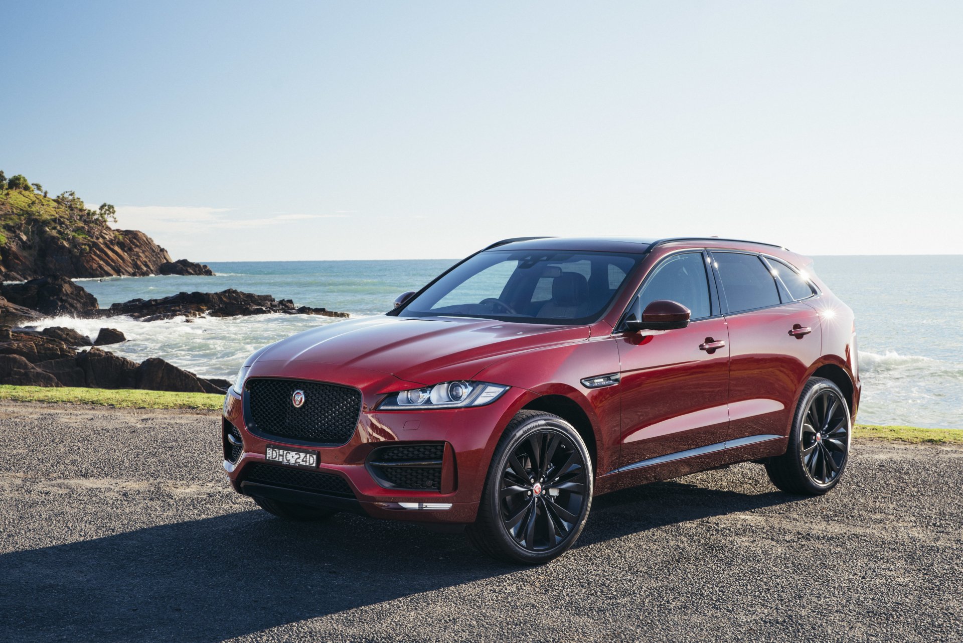 A red Jaguar F-PACE SUV parked by a coastal road with ocean and rocky cliffs in the background, captured in 4K Ultra HD for a PC desktop wallpaper.