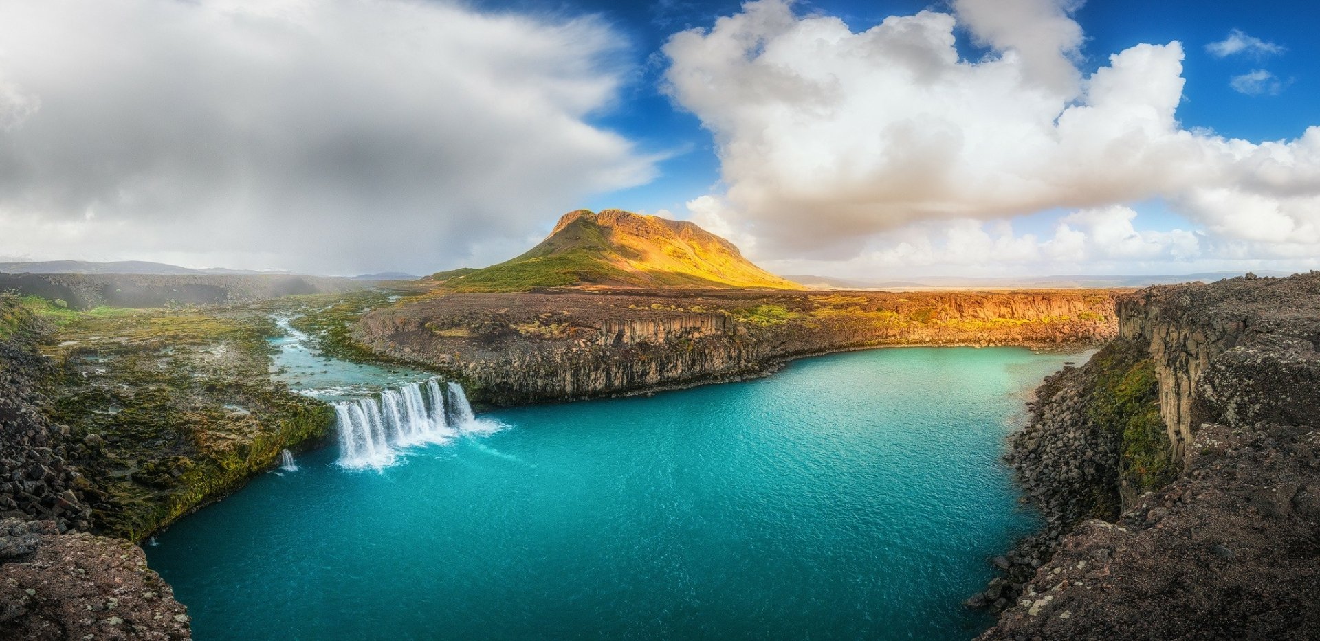 Stunning HD landscape of Iceland's Goðafoss waterfall cascading into a turquoise river, surrounded by rugged mountains and dramatic clouds.