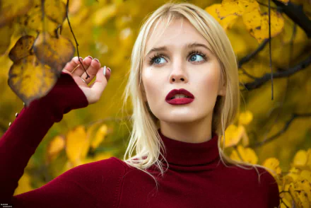 HD desktop wallpaper of a blonde woman with blue eyes and bold lipstick, posing against a backdrop of vibrant yellow autumn leaves.