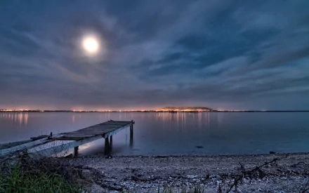 A serene night scene featuring a wooden pier and dock extending over a calm lake, illuminated by a bright full moon, surrounded by soft clouds and gentle water reflections.