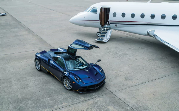 A sleek blue Pagani Huayra supercar with gullwing doors open, parked next to a private jet on a concrete runway, featured as an HD PC desktop wallpaper.