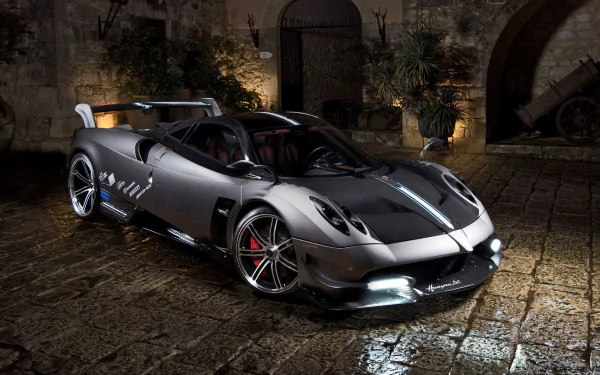HD wallpaper of a Pagani Huayra Roadster BC, showcasing the sleek, high-performance design of this supercar parked in a dimly lit, cobblestone courtyard.