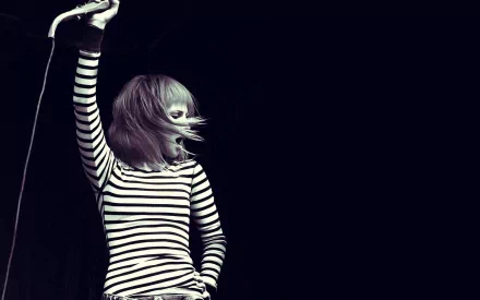 HD desktop wallpaper featuring a cute image of Hayley Williams from Paramore performing, with dynamic movement and a black and white striped outfit against a dark background.