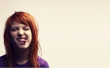 Close-up of Hayley Williams with vibrant orange hair, playfully sticking out her tongue, set against a simple background—a bold music-themed HD desktop wallpaper.