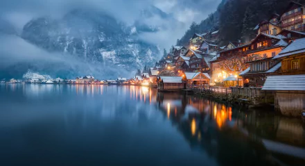 Winter evening view of Hallstatt, Austria, with houses reflecting on a serene lake, fog-shrouded mountains in the background. HD wallpaper showcasing a tranquil, picturesque man-made lakeside scene.
