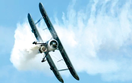 A dynamic biplane aircraft performs an aerial maneuver, leaving a trail of smoke against a clear blue sky. This HD image serves as a captivating desktop wallpaper.