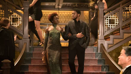 Chadwick Boseman as Black Panther in an elegant scene from the movie. The HD desktop wallpaper features him confidently walking down a grand staircase, arm-in-arm with a woman.