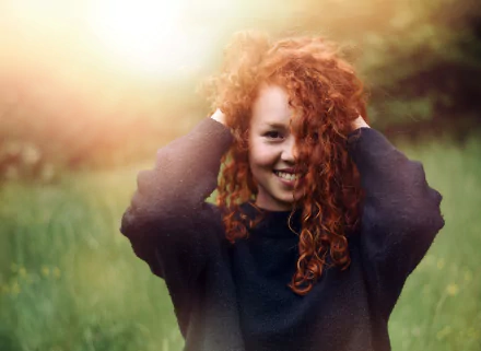 Sunny outdoor portrait of a smiling redhead woman with curly hair, captured in vibrant HD quality as a PC desktop wallpaper background.