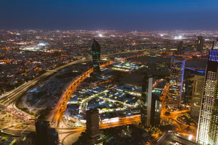 Aerial night view of Kuwait City's illuminated skyline with skyscrapers, glowing city lights, and a clear horizon, captured in HD for a vibrant cityscape wallpaper.