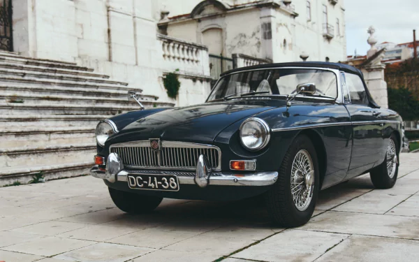 HD desktop wallpaper featuring a classic MG car parked in front of historic stone steps and buildings.