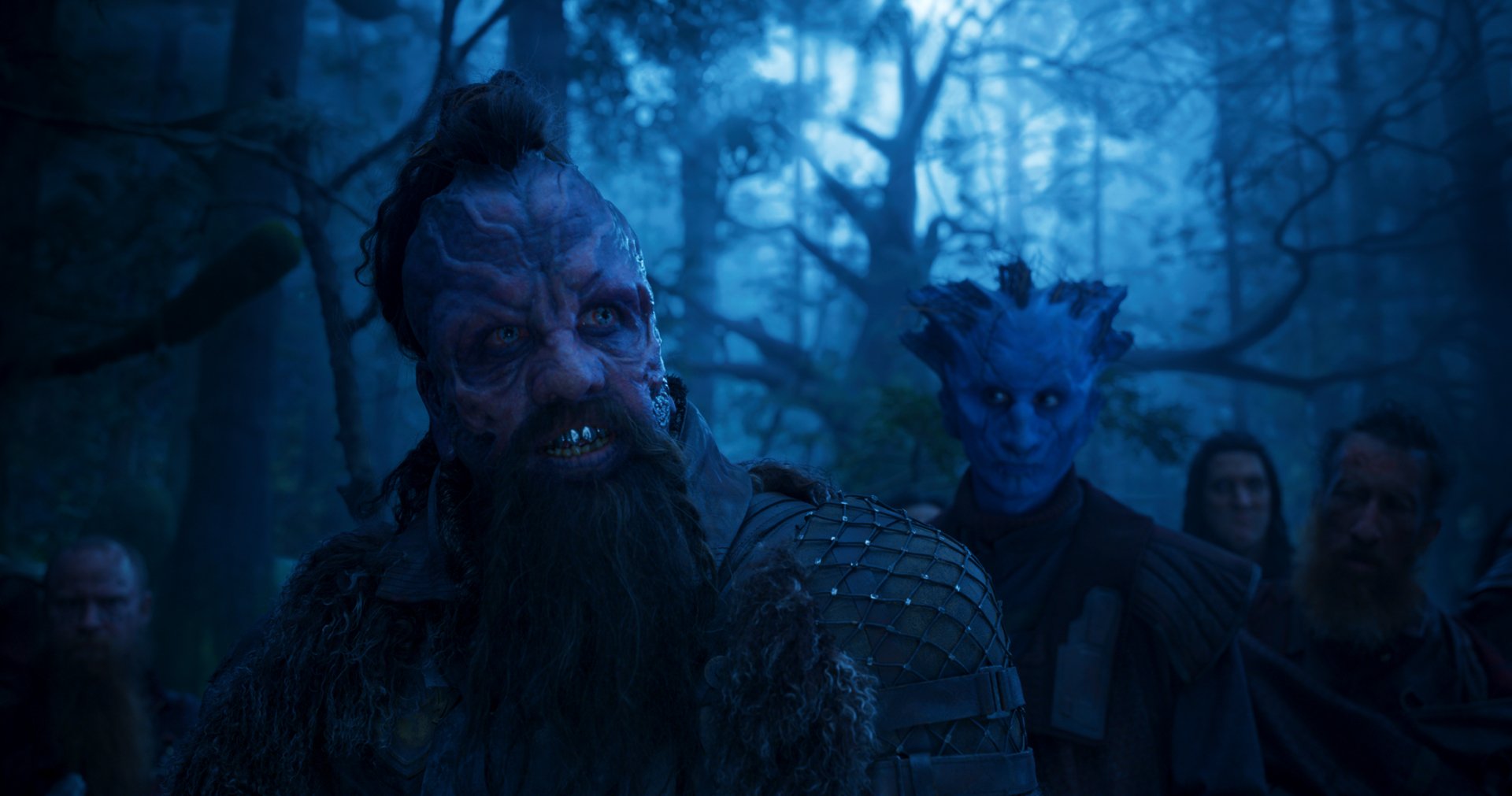 HD PC desktop wallpaper from Guardians of the Galaxy Vol. 2 — bearded, tattooed alien leader in a misty blue forest, blue-skinned companion and shadowed figures behind.