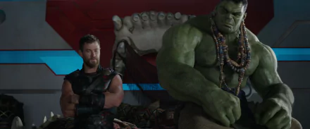 Thor and Hulk sit together in a scene from Thor: Ragnarok. This HD wallpaper shows Thor in black armor and Hulk adorned with necklaces against a backdrop of vibrant, futuristic elements.