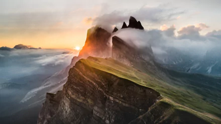 A stunning HD desktop wallpaper of a mountain peak enveloped in clouds and fog, with sunbeams piercing through during sunset, highlighting the natural beauty.