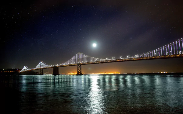 A 4K Ultra HD night view of San Francisco's Bay Bridge illuminated with lights, reflecting beautifully on the water beneath a starry sky.