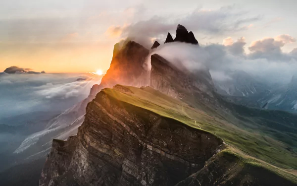 A stunning HD desktop wallpaper of a mountain peak enveloped in clouds and fog, with sunbeams piercing through during sunset, highlighting the natural beauty.