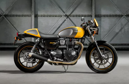 Side view of a yellow-and-gray Triumph Street Cup motorcycle, a classic Triumph vehicle, parked in an industrial garage — high-resolution 2K Quad HD PC desktop wallpaper/background.
