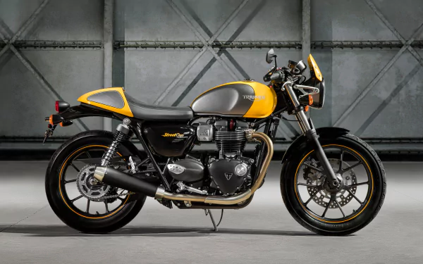 Side view of a yellow-and-gray Triumph Street Cup motorcycle, a classic Triumph vehicle, parked in an industrial garage — high-resolution 2K Quad HD PC desktop wallpaper/background.