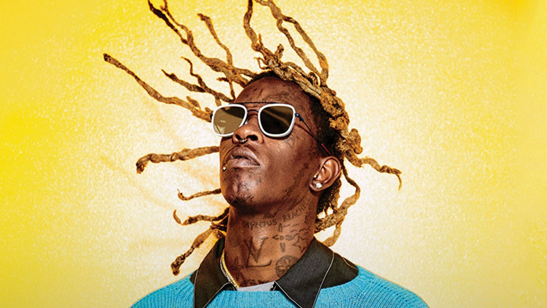 HD desktop wallpaper featuring a person with sunglasses and dynamic dreadlocks against a vibrant yellow background.