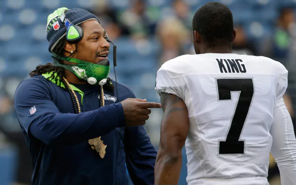 Marshawn Lynch interacts with a teammate before a game, showcasing the camaraderie of the Seattle Seahawks. A vibrant HD wallpaper capturing sportsmanship and teamwork.
