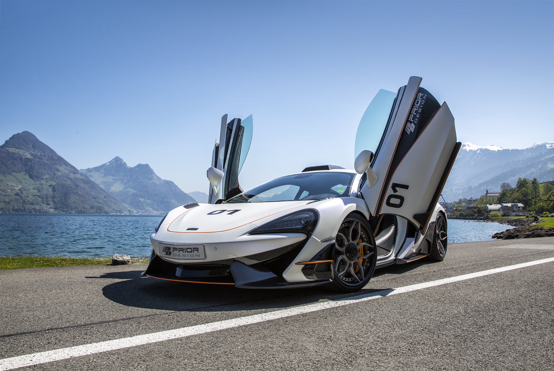White McLaren 570S supercar with butterfly doors open, parked by a lakeside road with mountains in the background; HD PC desktop wallpaper showcasing the sleek vehicle.