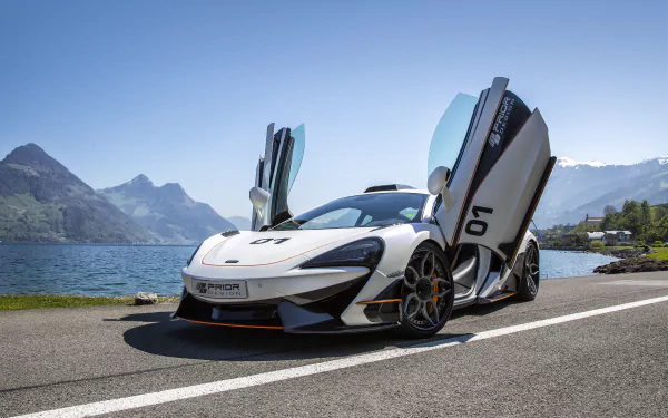 White McLaren 570S supercar with butterfly doors open, parked by a lakeside road with mountains in the background; HD PC desktop wallpaper showcasing the sleek vehicle.
