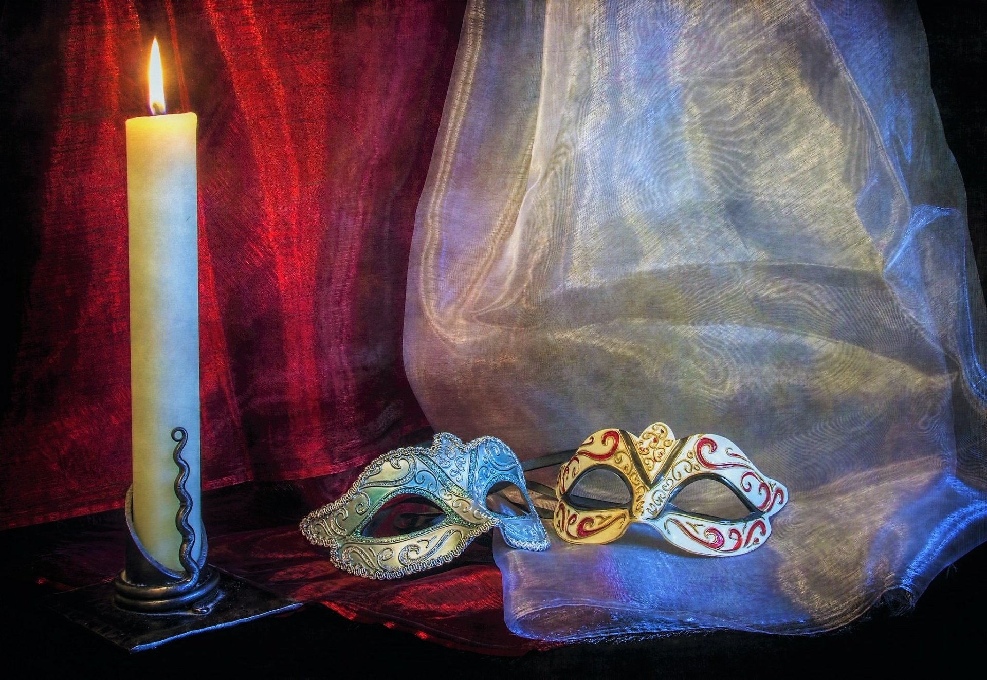 HD desktop wallpaper still life: lit candle beside two ornate Venetian masks on draped red and sheer curtains, warm flame glow.