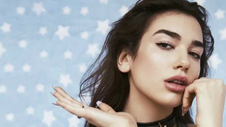 HD desktop wallpaper and background of Dua Lipa with a blue starry background. The singer poses confidently with her hand near her chin, exuding a stylish and elegant aura.