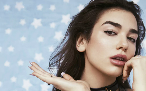 HD desktop wallpaper and background of Dua Lipa with a blue starry background. The singer poses confidently with her hand near her chin, exuding a stylish and elegant aura.