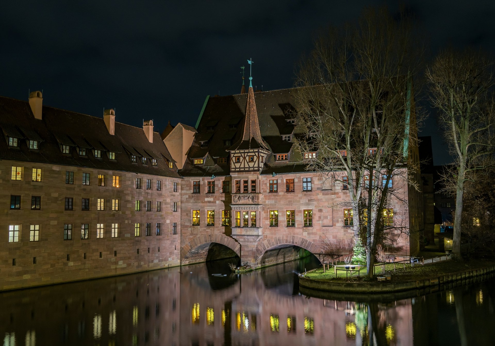 Night view of a historic German building housing a restaurant, illuminated and reflecting on the calm water, captured in 4K Ultra HD for a PC desktop wallpaper.
